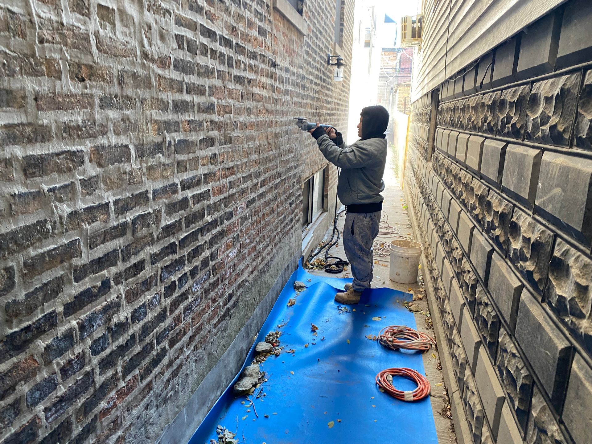 A man is working on a brick wall in an alleyway.