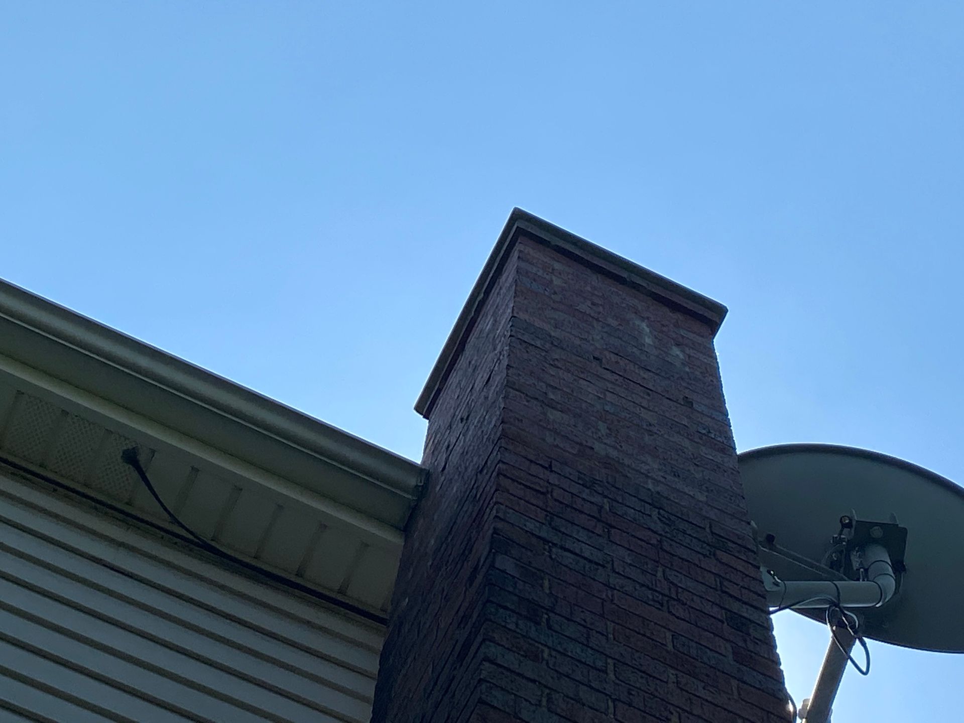 A brick chimney with a satellite dish attached to it.
