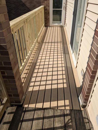 A wooden deck is sitting on the side of a brick house.
