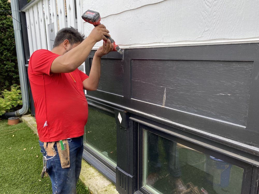 A man in a red shirt is using a hammer to fix a window.