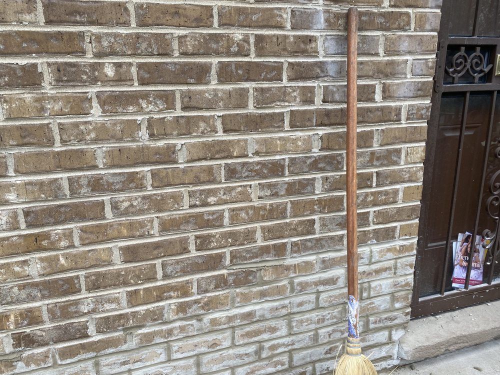 A broom is leaning against a brick wall.