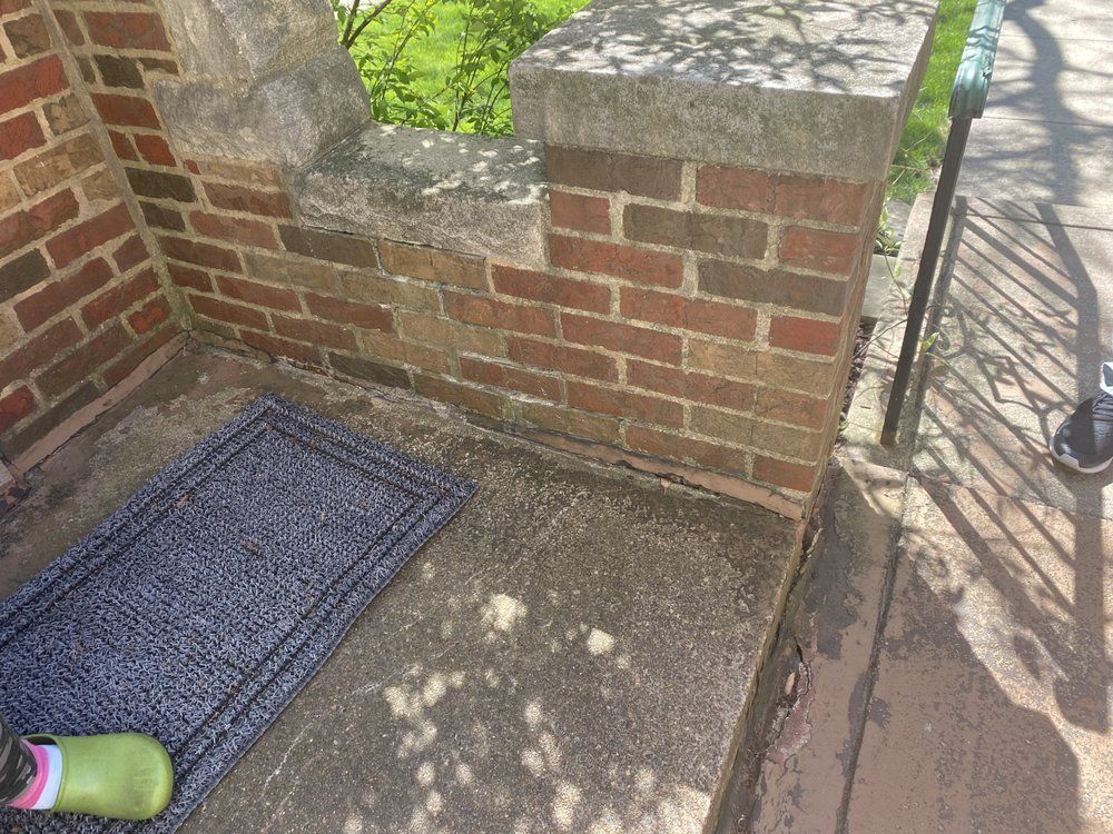 A door mat is sitting on a porch next to a brick wall.