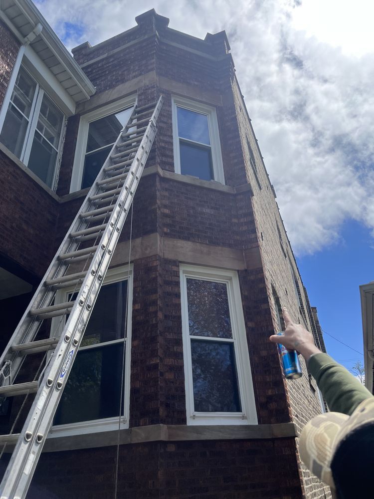 A person is pointing at a ladder on the side of a brick building.