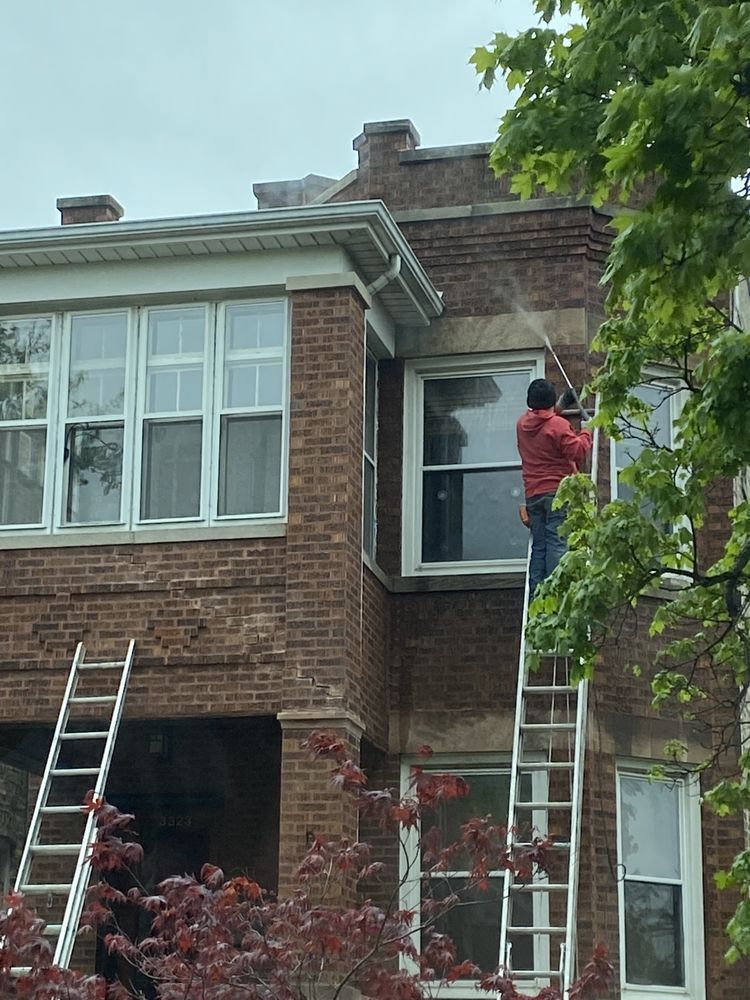 A man is standing on a ladder cleaning a brick building.