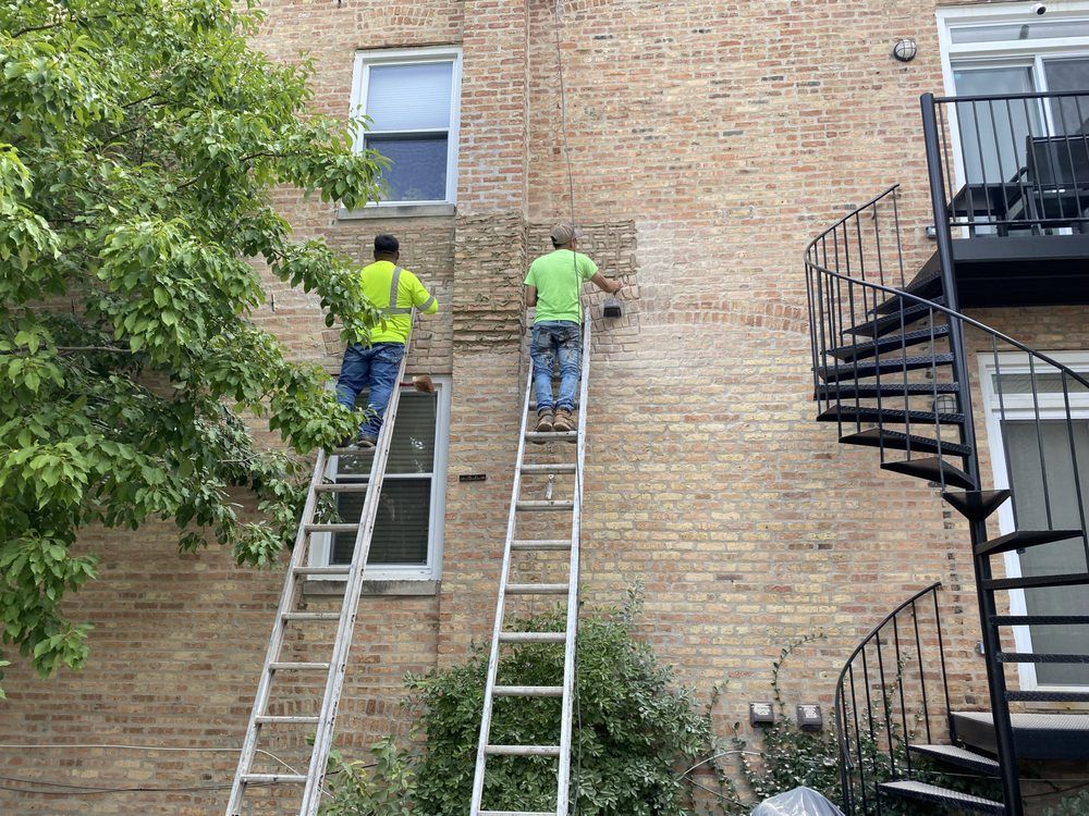 Two men are standing on ladders on the side of a brick building.