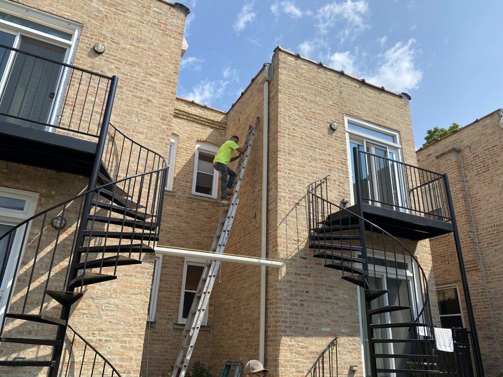 A man is climbing a ladder to paint a brick building.