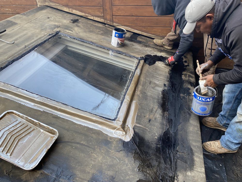A man is painting a skylight on a roof.