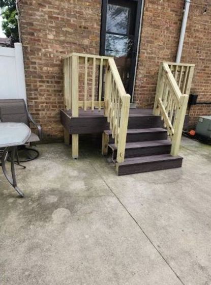 A wooden deck with stairs and a table in front of a brick building.