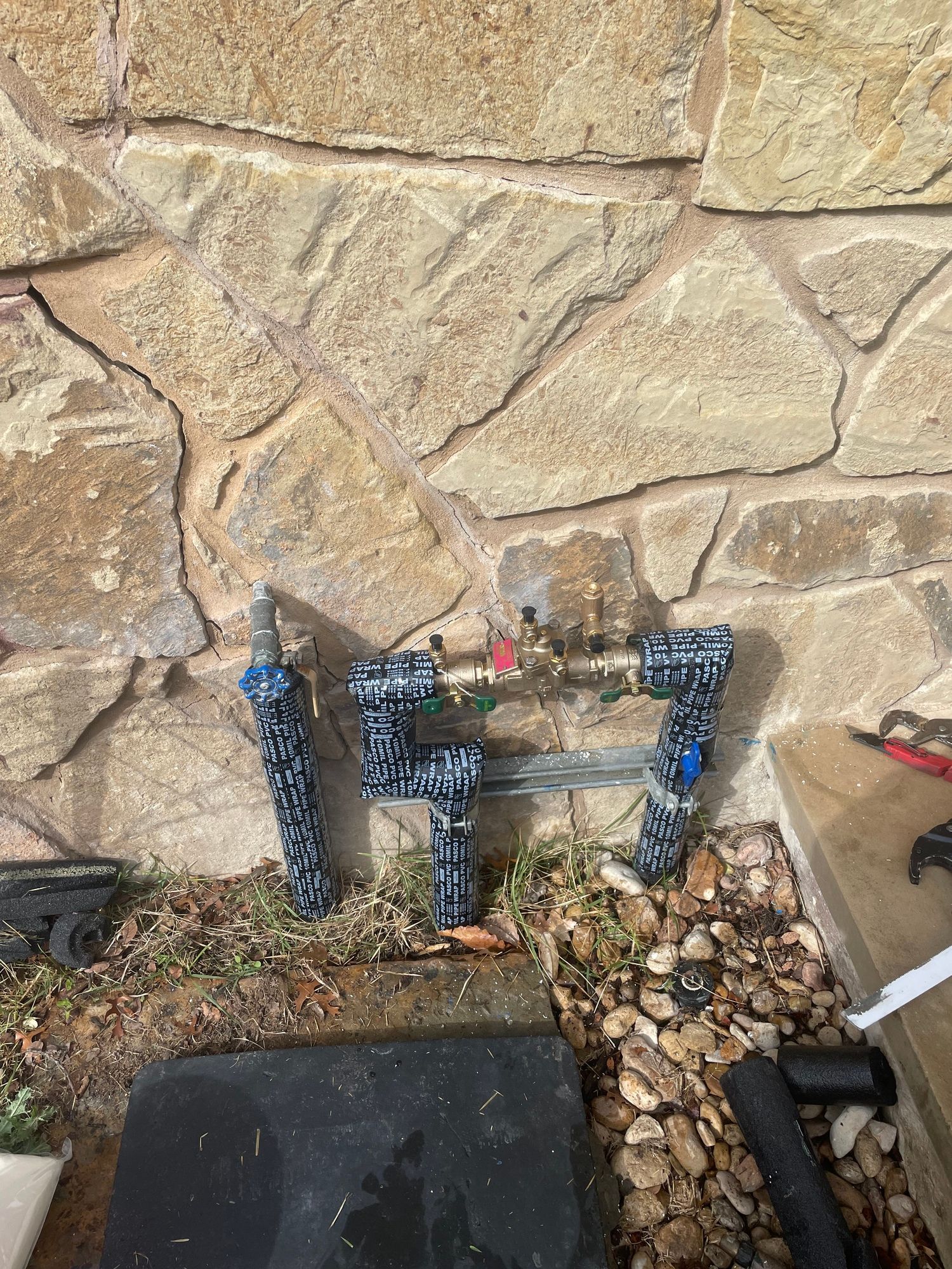 A faucet is sitting on the ground in front of a stone wall.