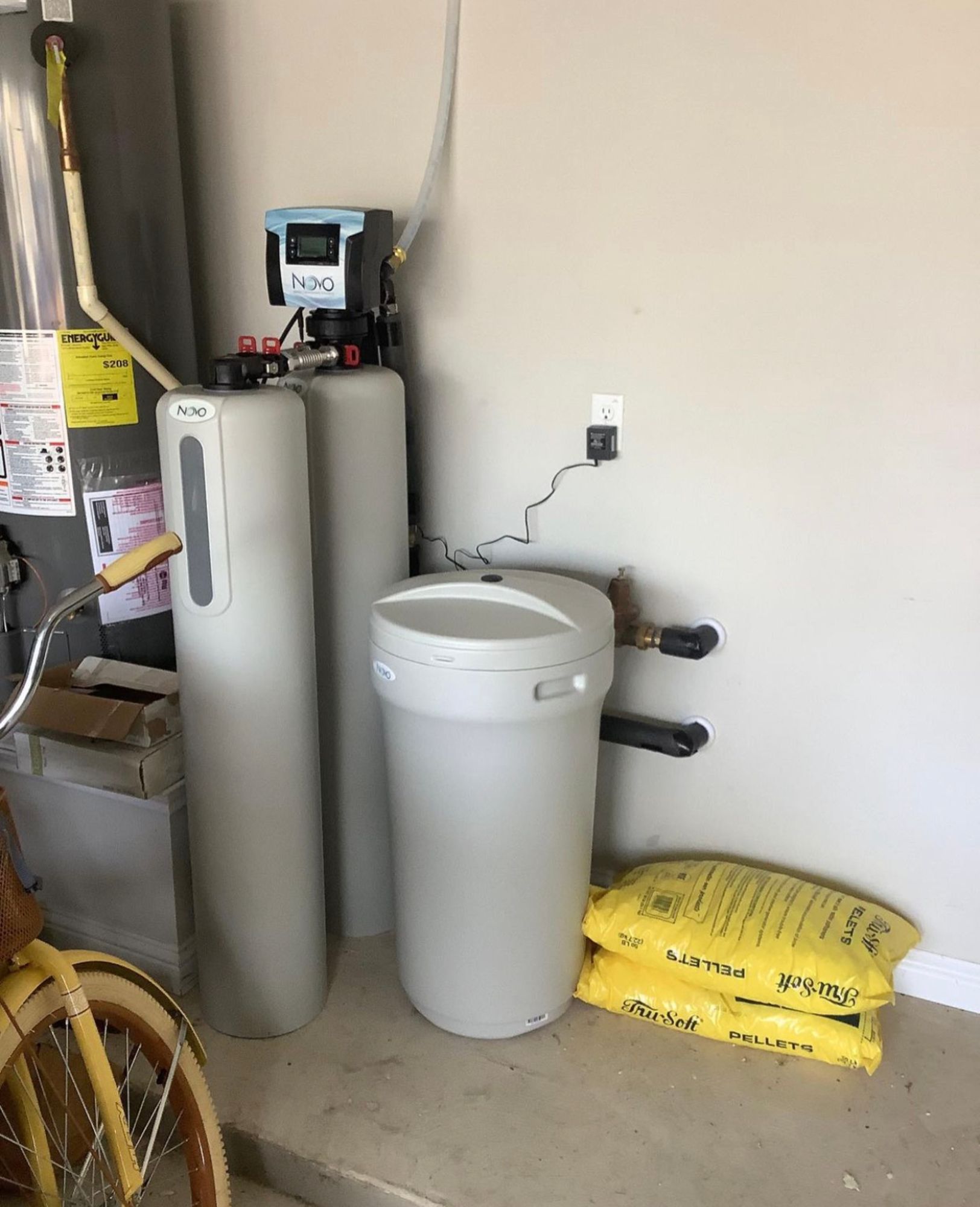 A water softener is sitting next to a water heater in a garage.
