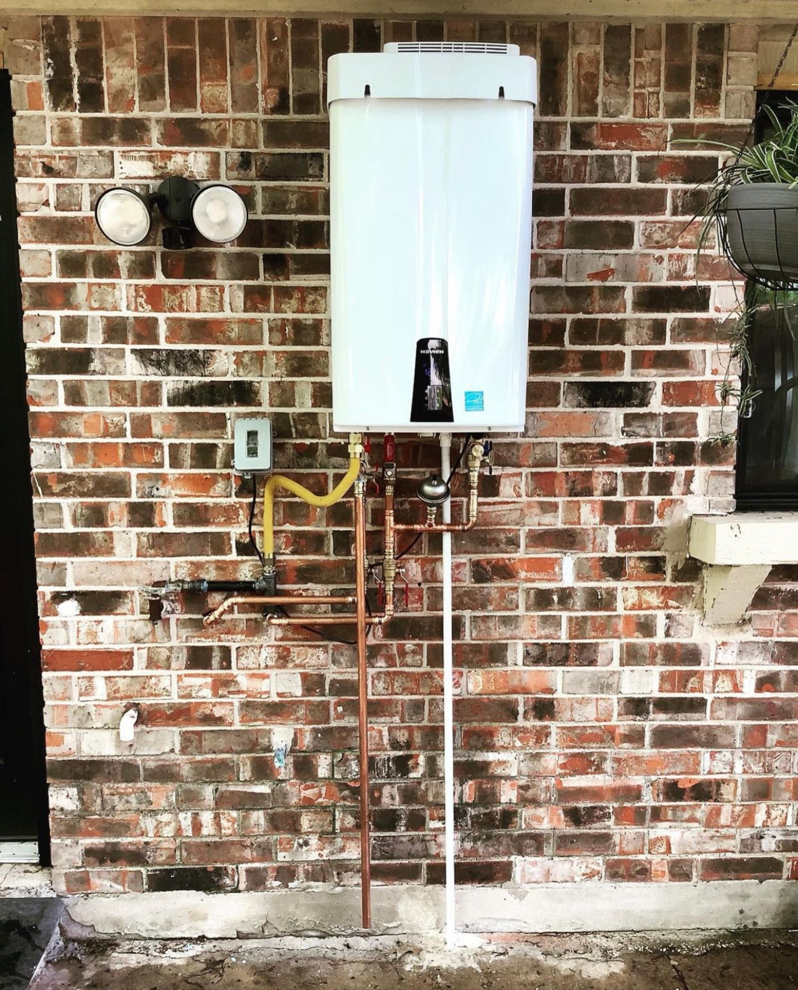 A white water heater is attached to a brick wall.