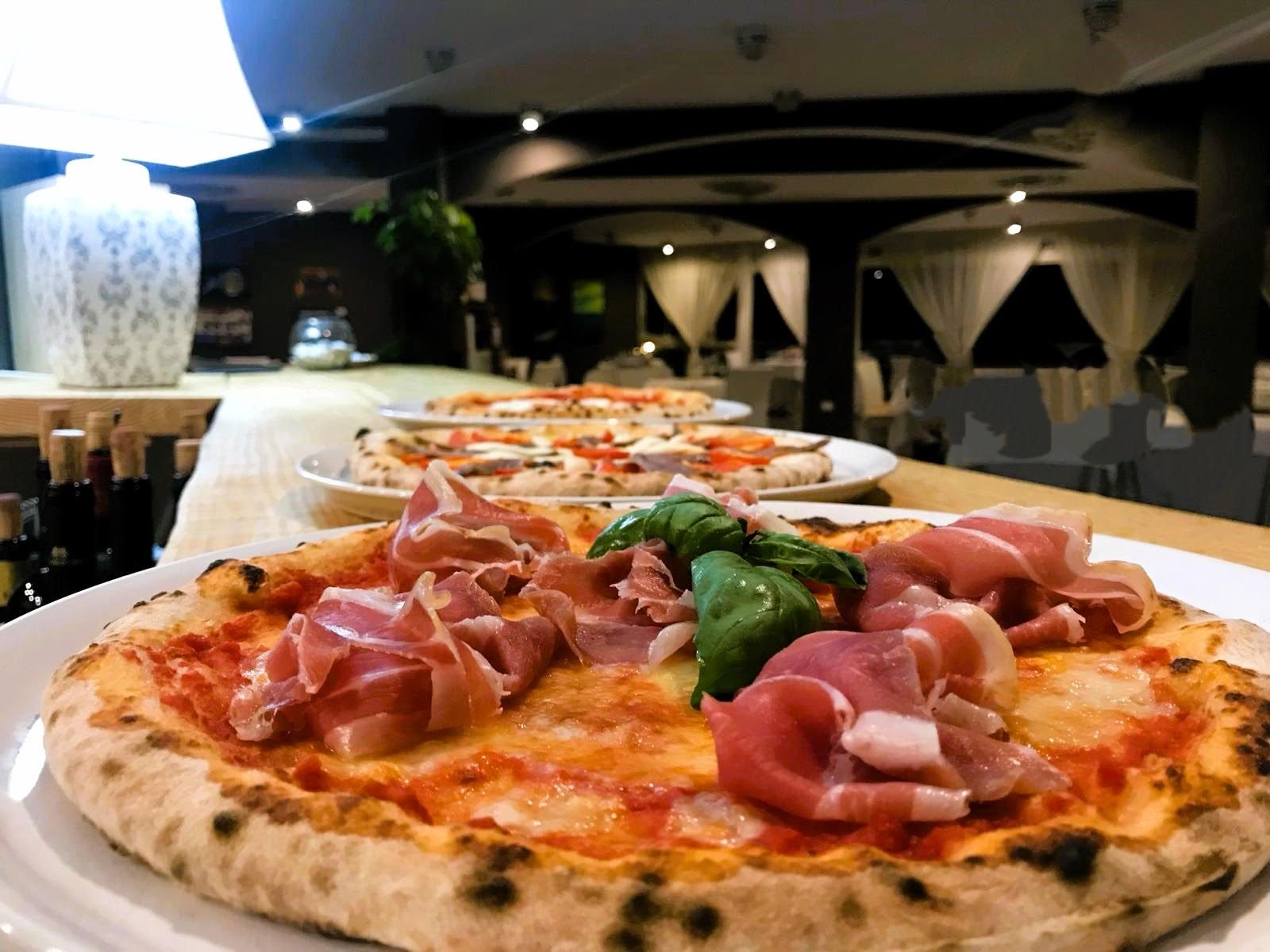 Una pizza con prosciutto e basilico è appoggiata su un piatto bianco su un tavolo.