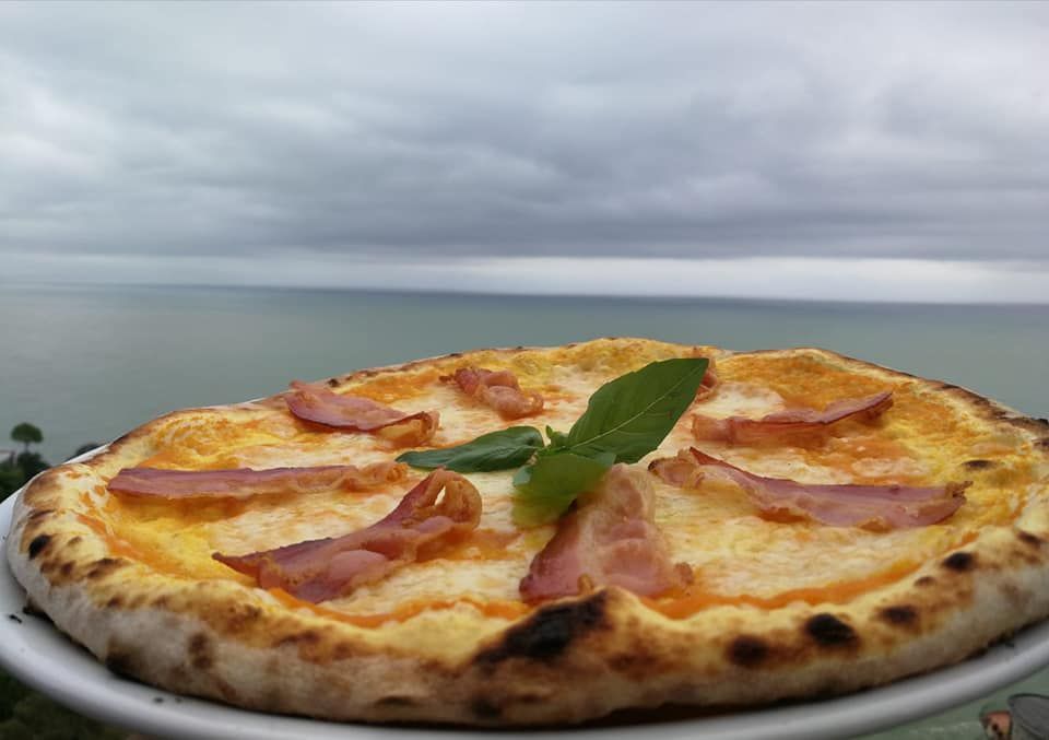 Una pizza con pancetta è su un piatto con l'oceano sullo sfondo.