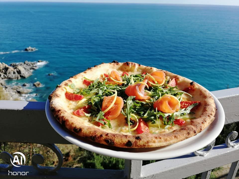 Una pizza è appoggiata su un piatto bianco su un balcone che si affaccia sull'oceano.