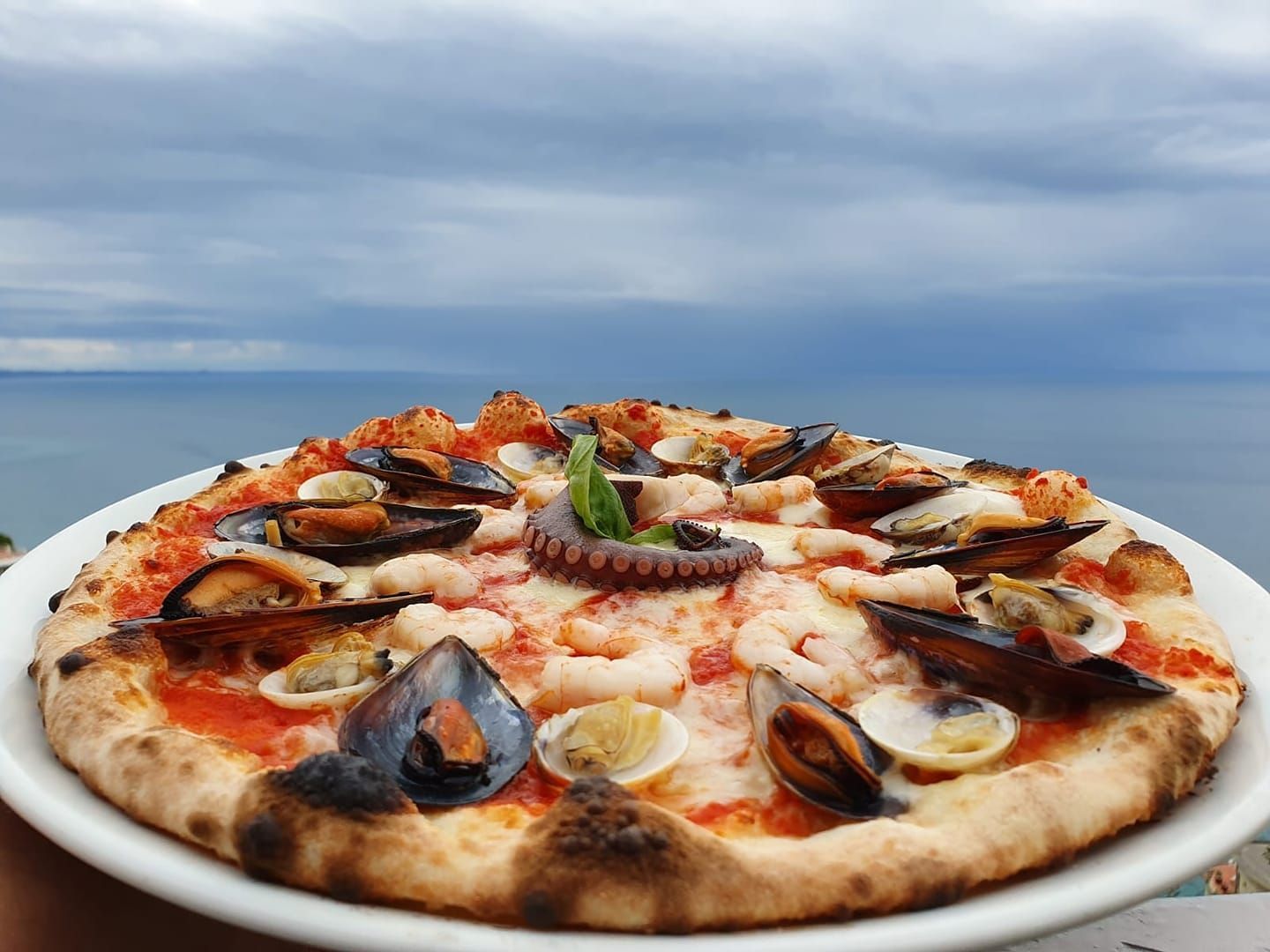 Una pizza con frutti di mare è su un piatto di fronte all'oceano.