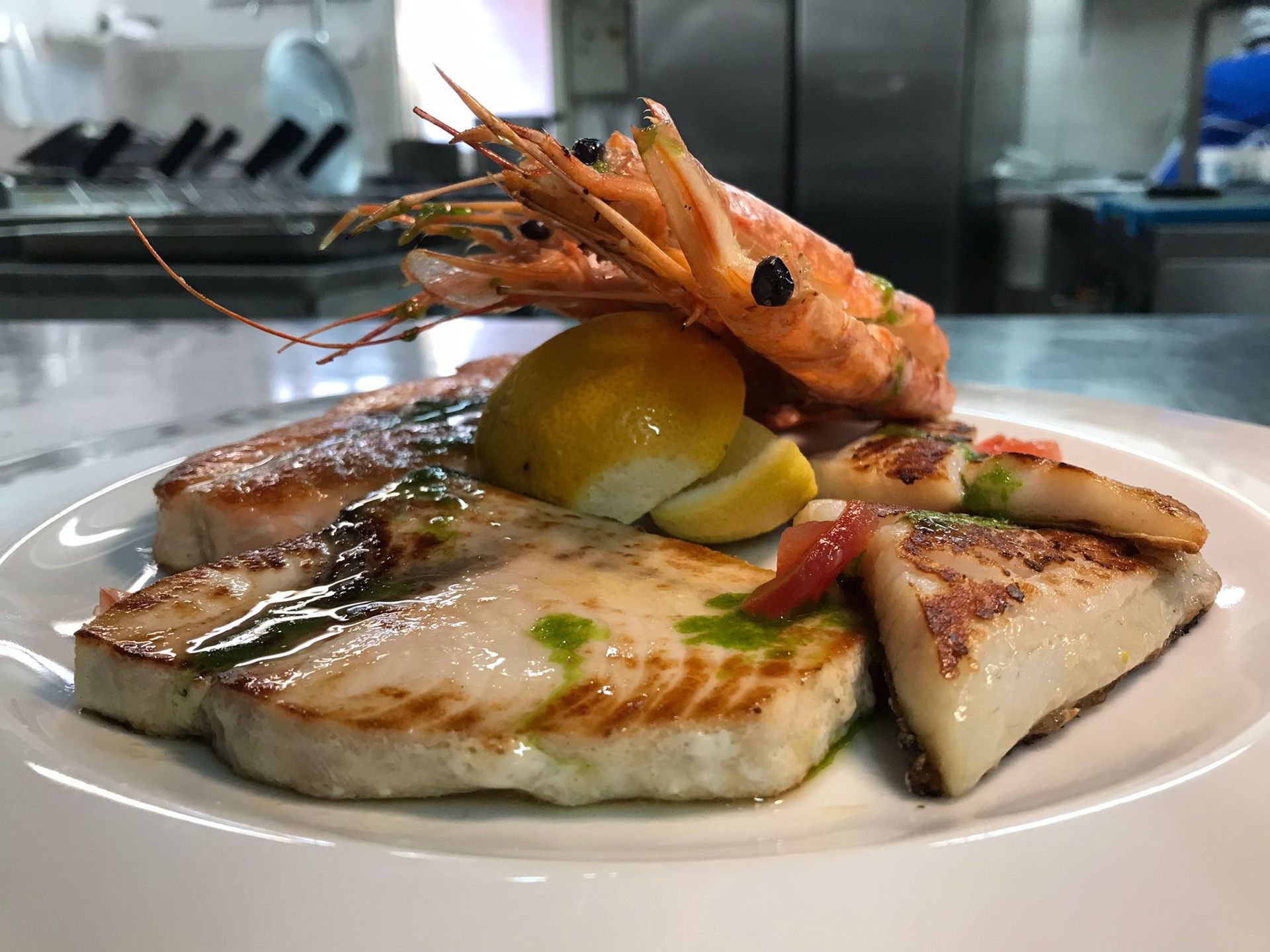 Un piatto bianco con sopra pesce e gamberi su un tavolo.