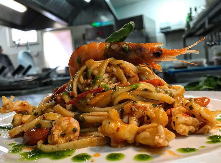 Un piatto bianco con sopra tagliatelle e gamberetti in una cucina.