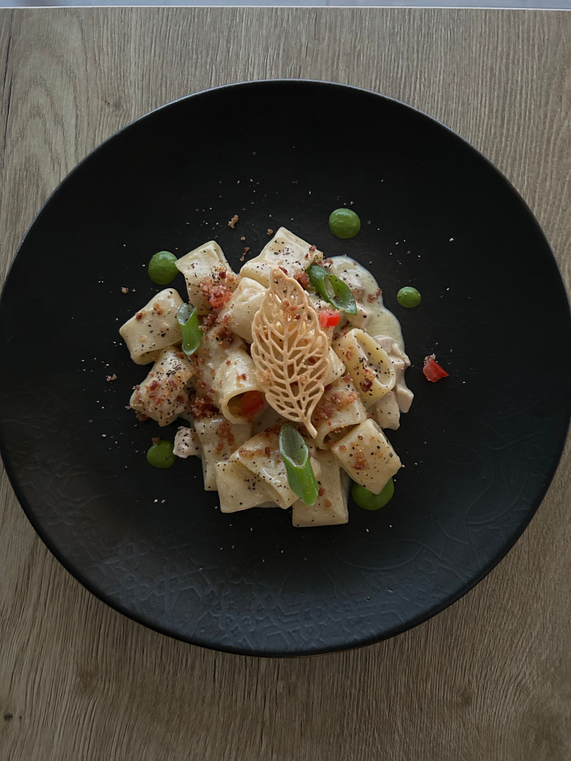 Un piatto nero con sopra pasta e verdure su un tavolo di legno.