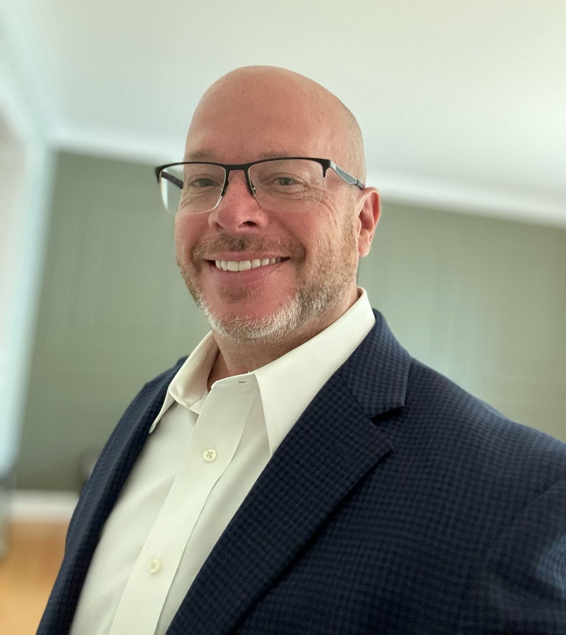 A bald man wearing glasses and a suit is smiling for the camera.