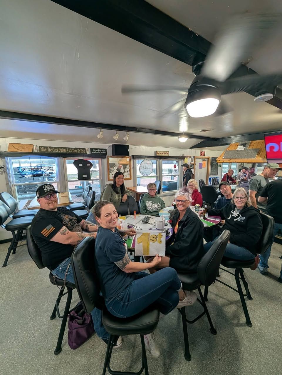 People seated at tables inside a casual restaurant, with drinks and a ceiling fan overhead.