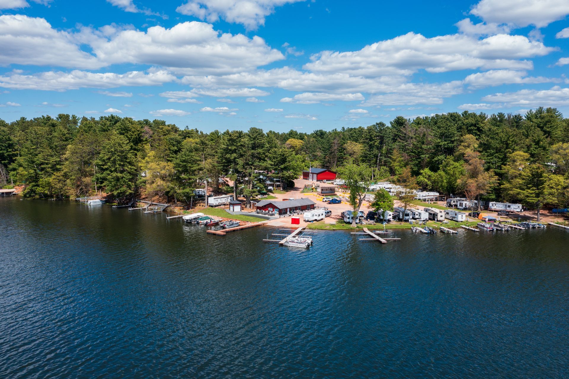 Lakeside campground with docks, boats, tents, and trees under a blue sky