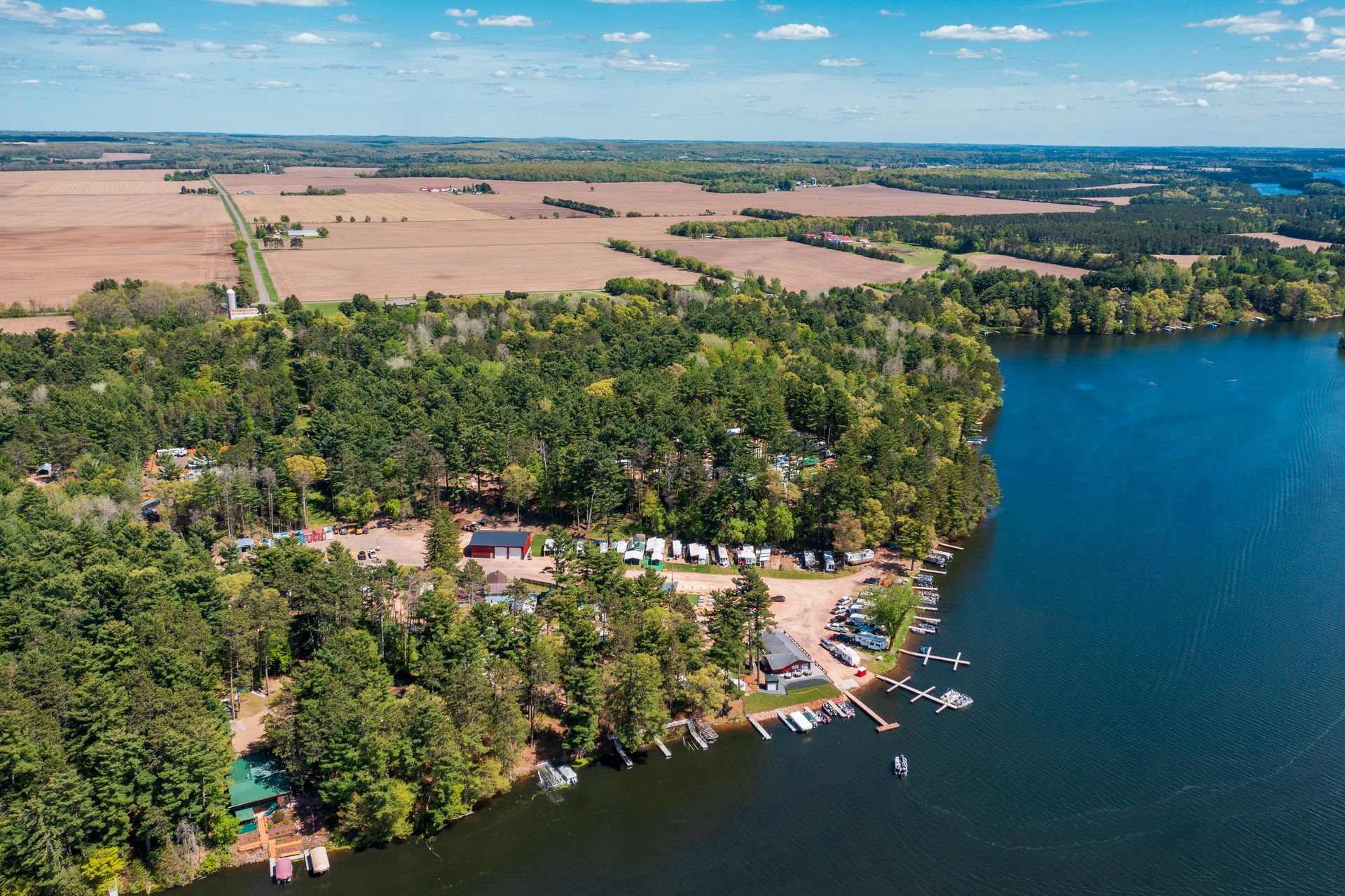 Aerial view of a lakeside resort with docks, trees, and farmland under a clear blue sky