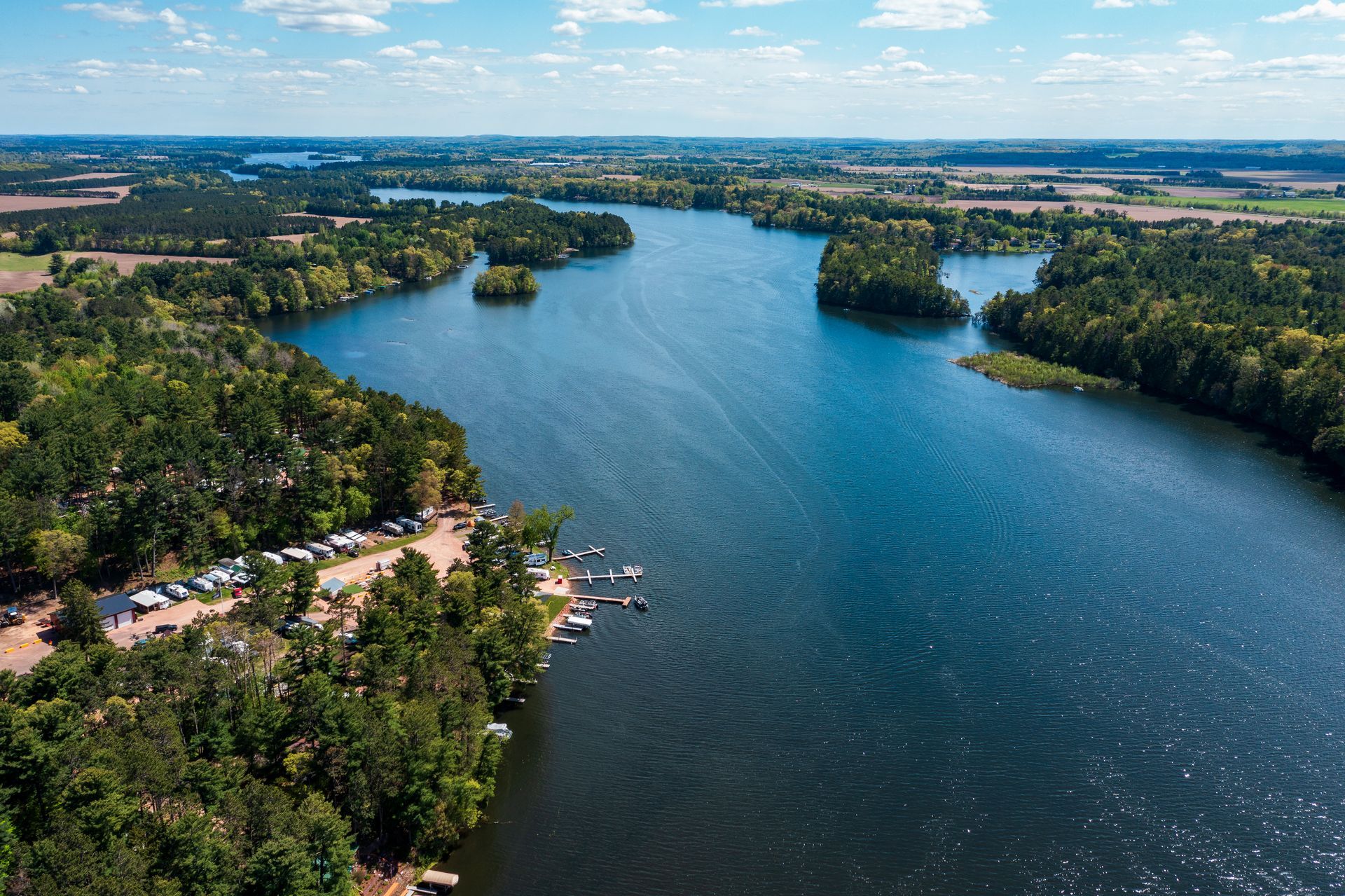 Aerial view of a winding blue river through dense green forest under a bright sky