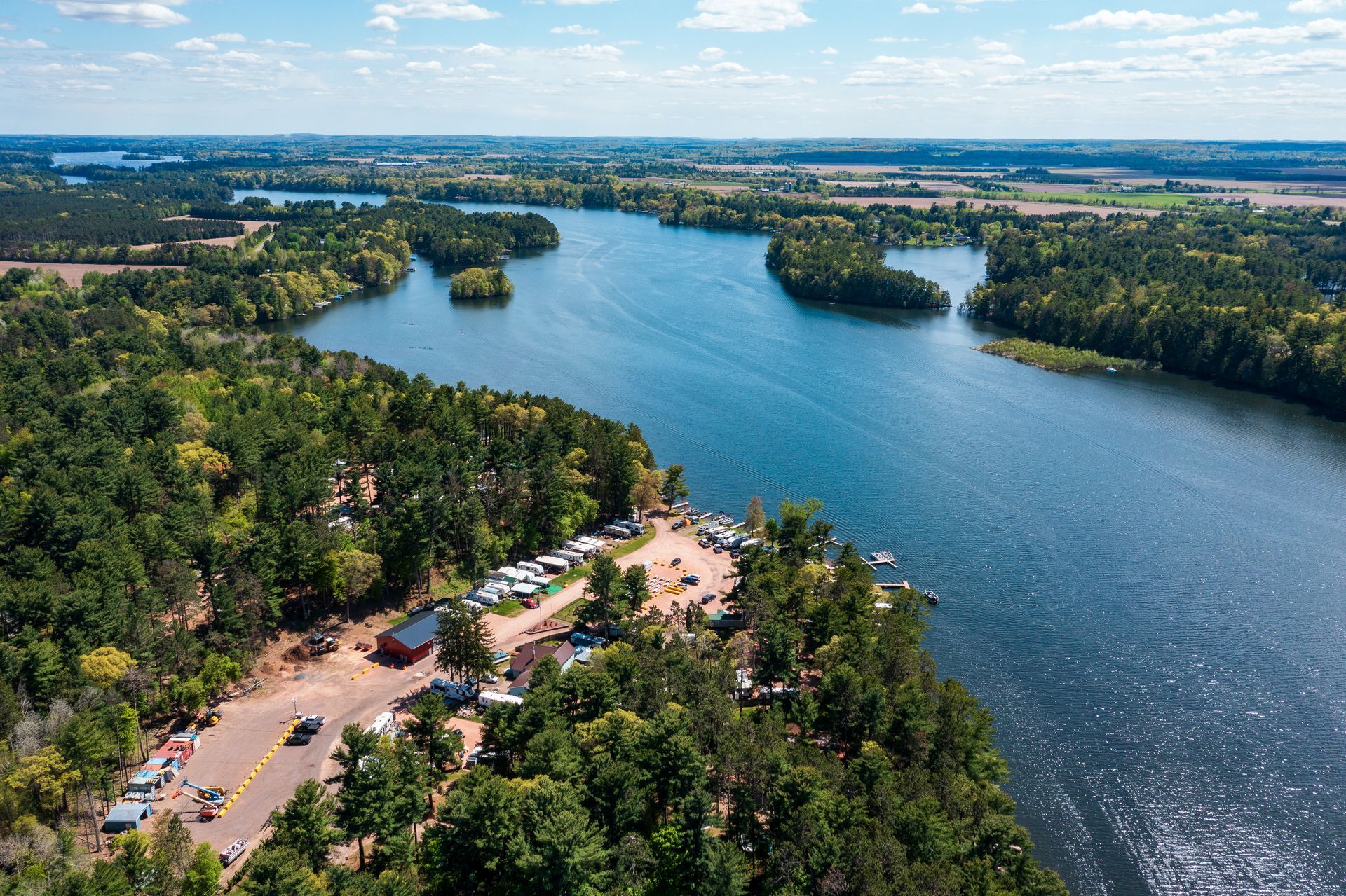 Aerial view of a wide river bordered by dense green forest and a small shoreline parking area