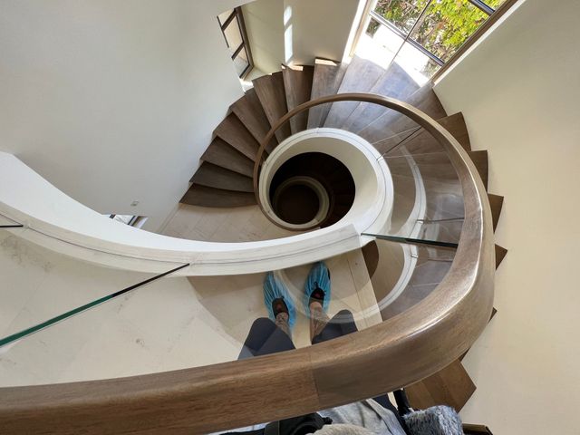 Spiral staircase viewed from above, with blue shoes visible on the steps and a windowed landing below