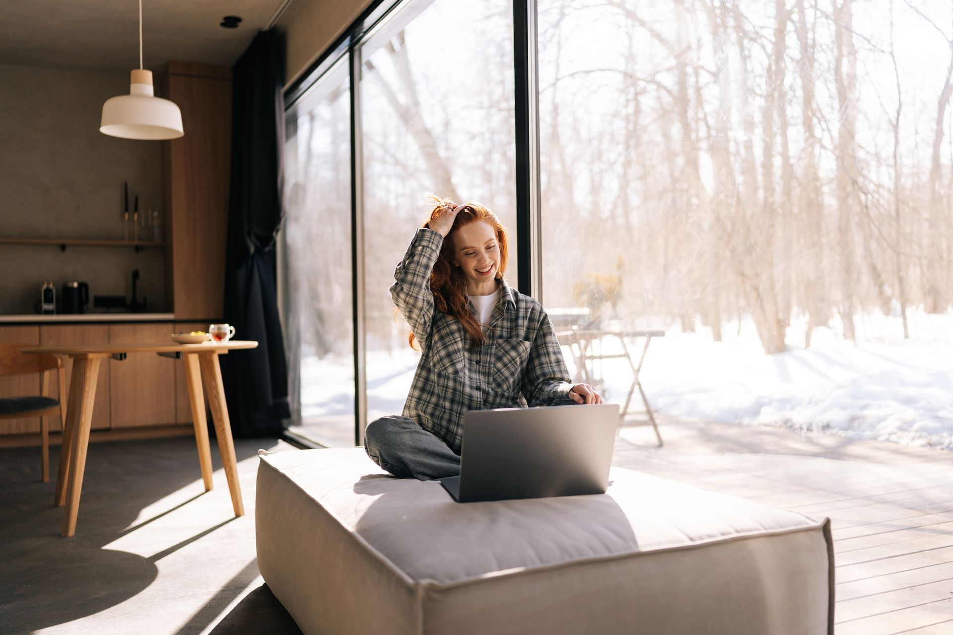 Person sitting on a cushioned bench with a laptop in a bright snowy cabin interior