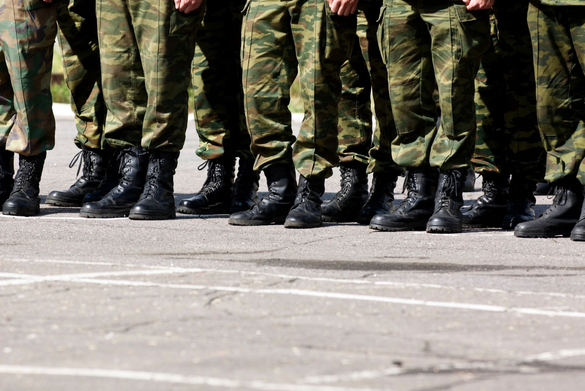 Row of soldiers in camouflage pants and black boots standing on pavement