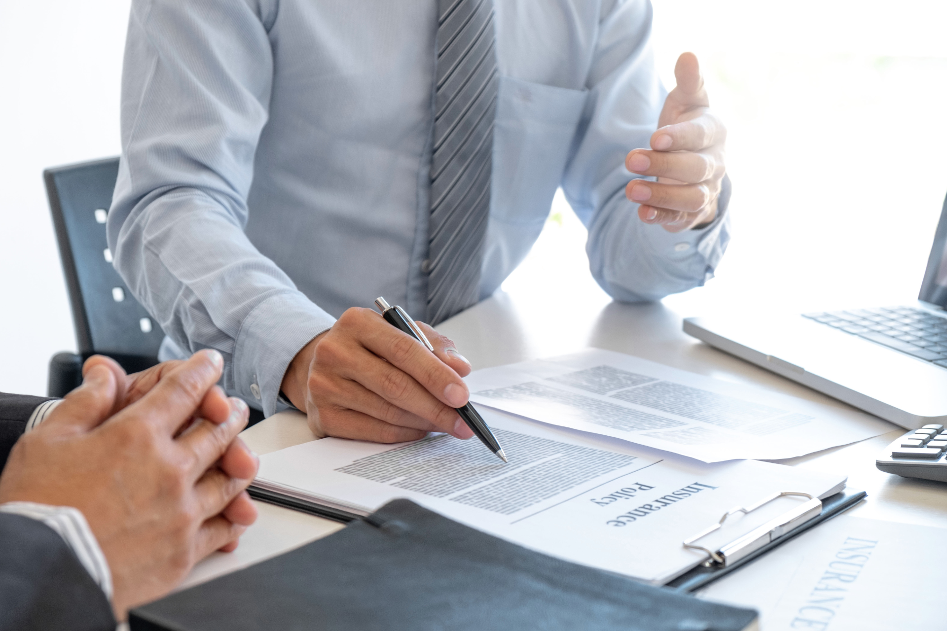 Two people signing documents at a desk with a laptop and pen in a bright office