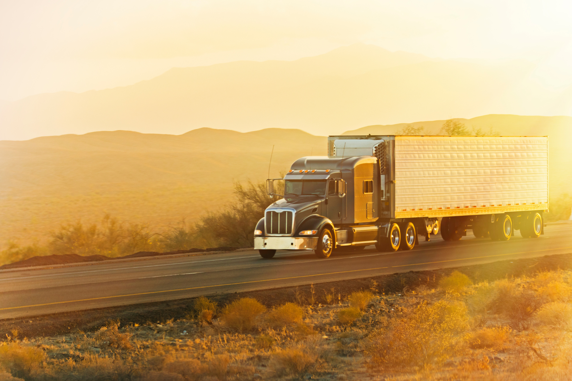 Semi-truck hauling a trailer on a desert highway at sunset