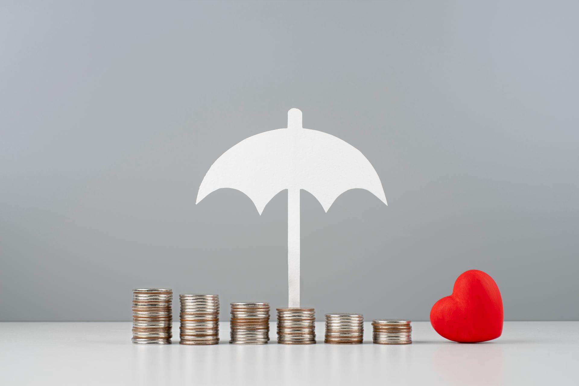 White umbrella over stacks of coins beside a red heart on a gray background