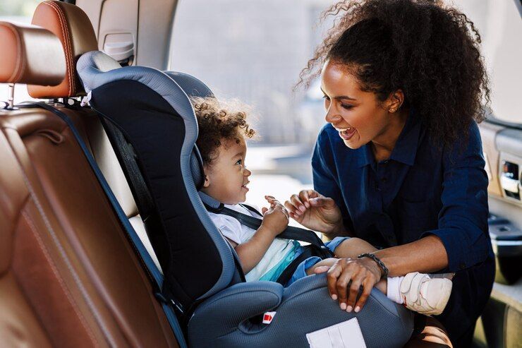 Woman fastening a child in a car seat inside a vehicle, with both smiling