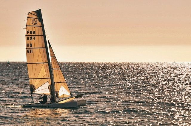 Sailboat with tan sails gliding on sunlit ocean at sunset