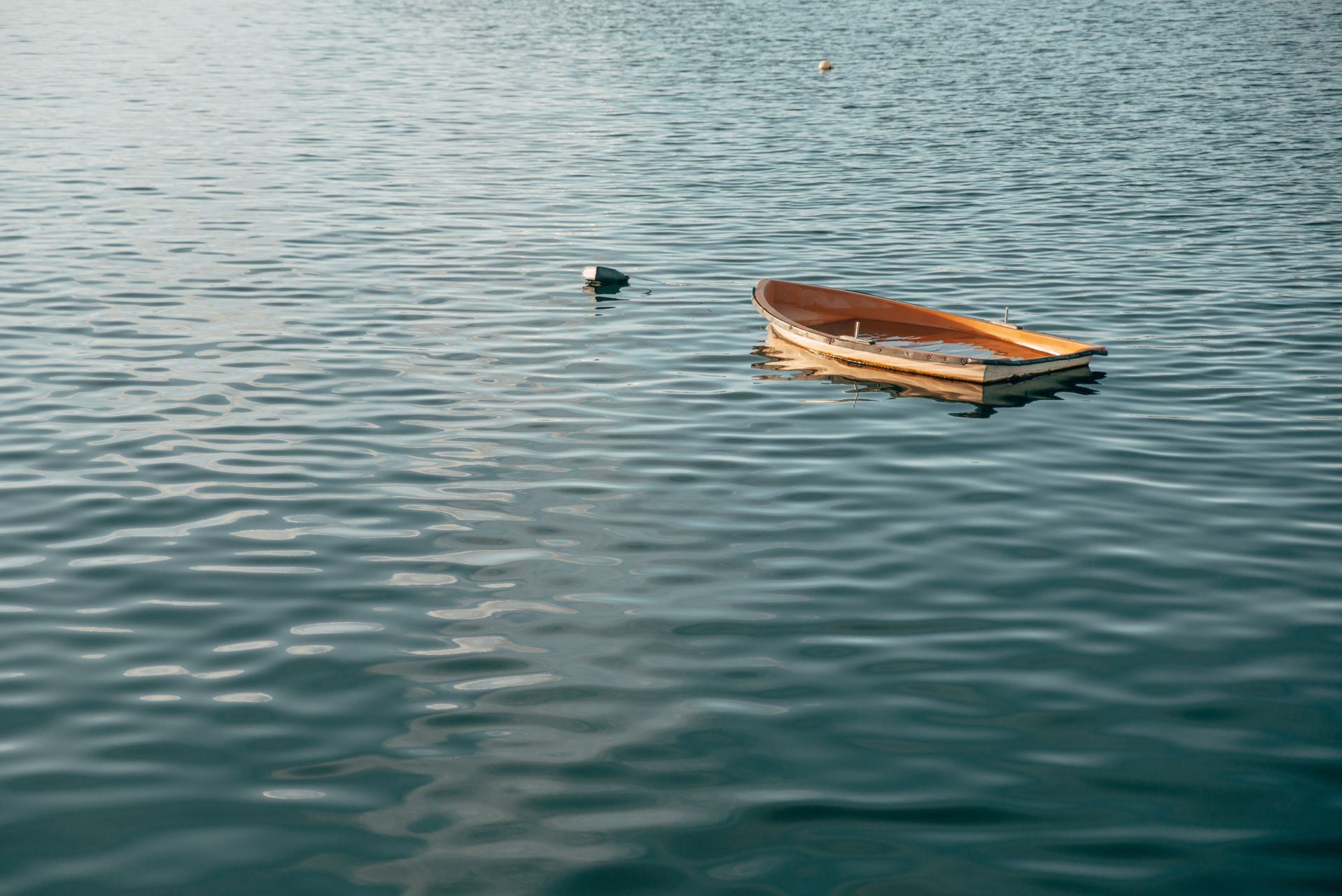 Small wooden boat floating on calm blue water with a dark buoy nearby.