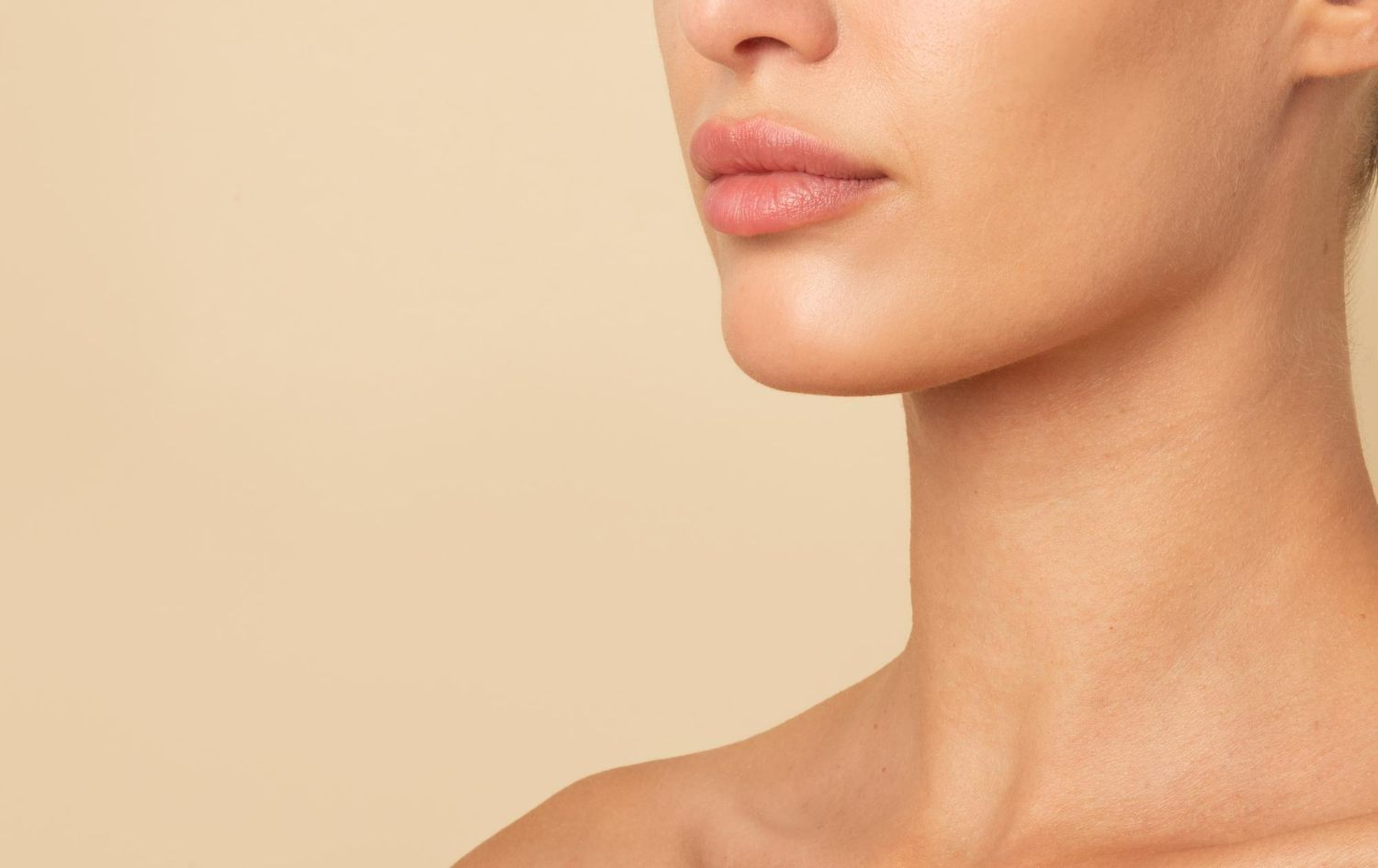 A close-up of a person's lower face and neck against a light beige background.
