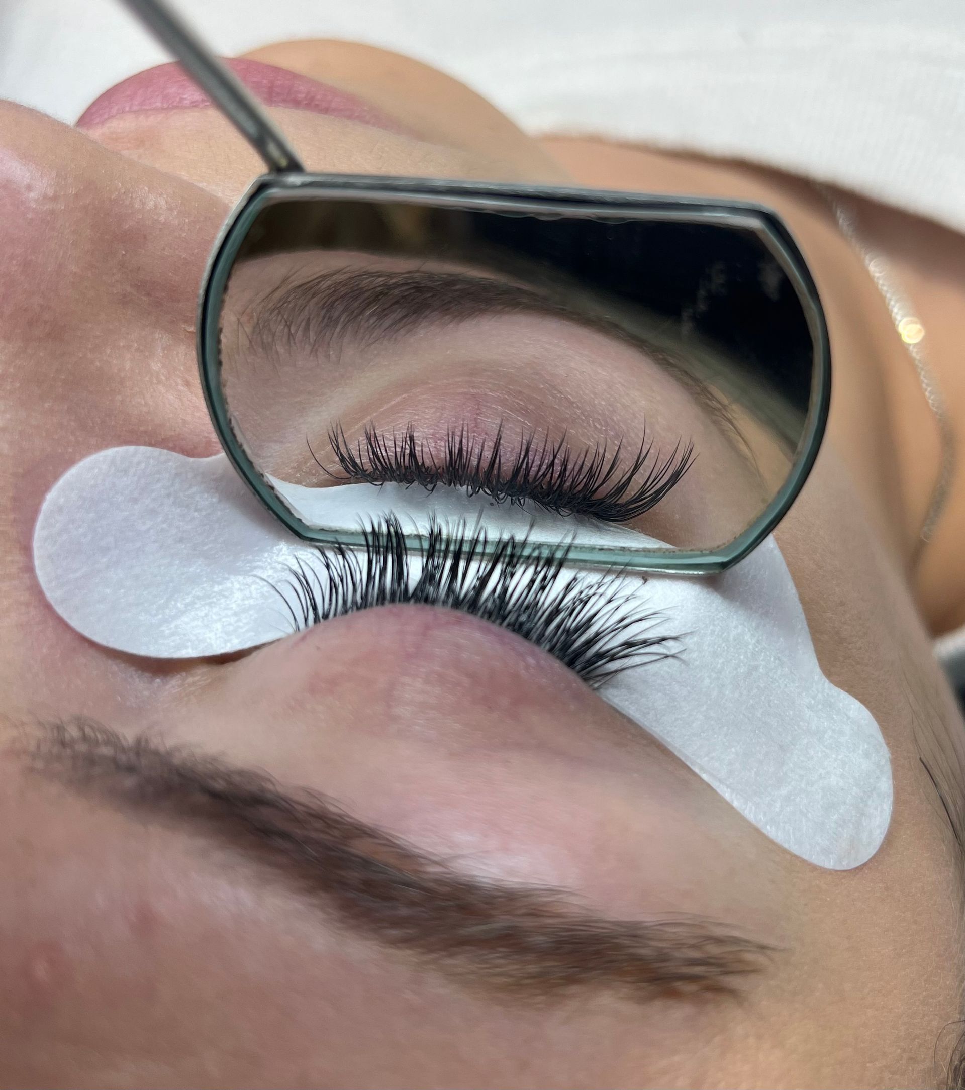 Close-up of eyelash extensions being applied with under-eye pads and a small mirror overhead