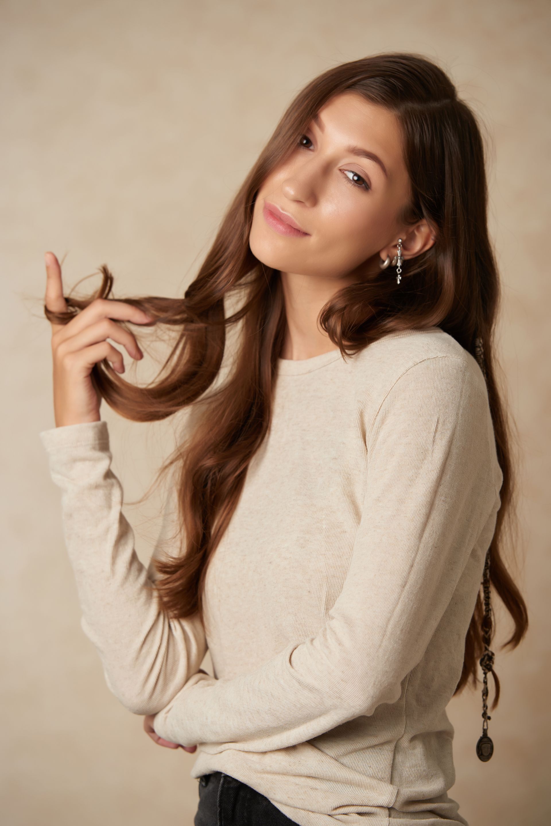 A woman in a white sweater is holding her hair.
