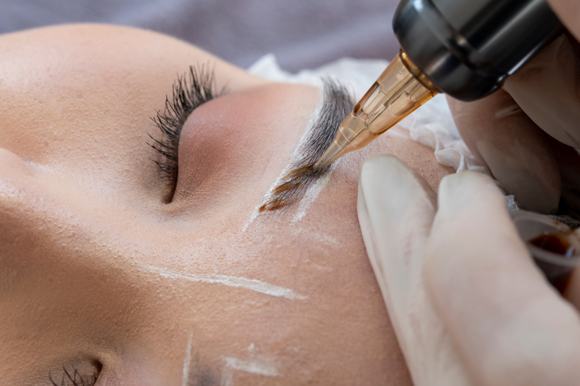 A woman is getting a permanent makeup tattoo on her eyebrows.
