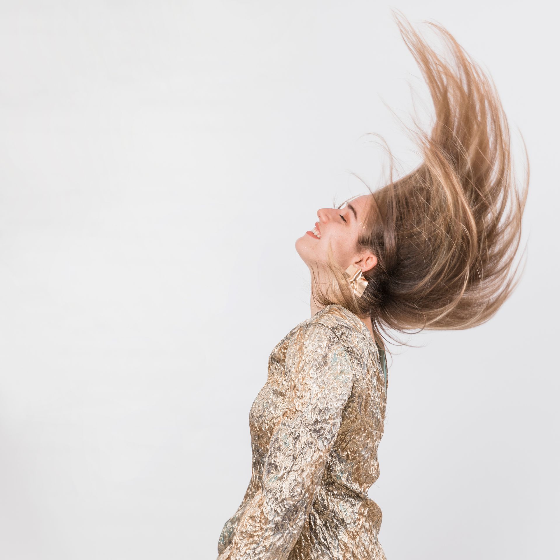 A woman in a gold dress is throwing her hair in the air.