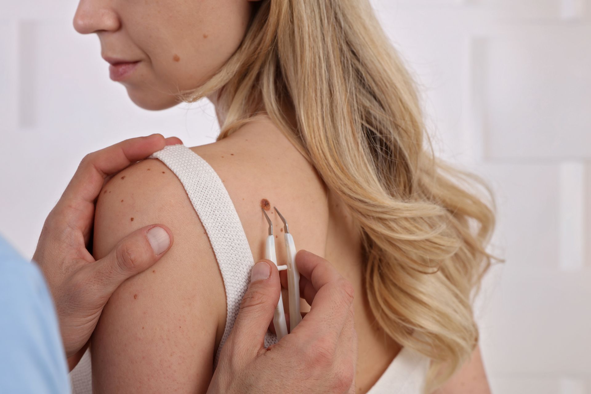 A person's shoulder being examined with medical tools by a person in a blue shirt.