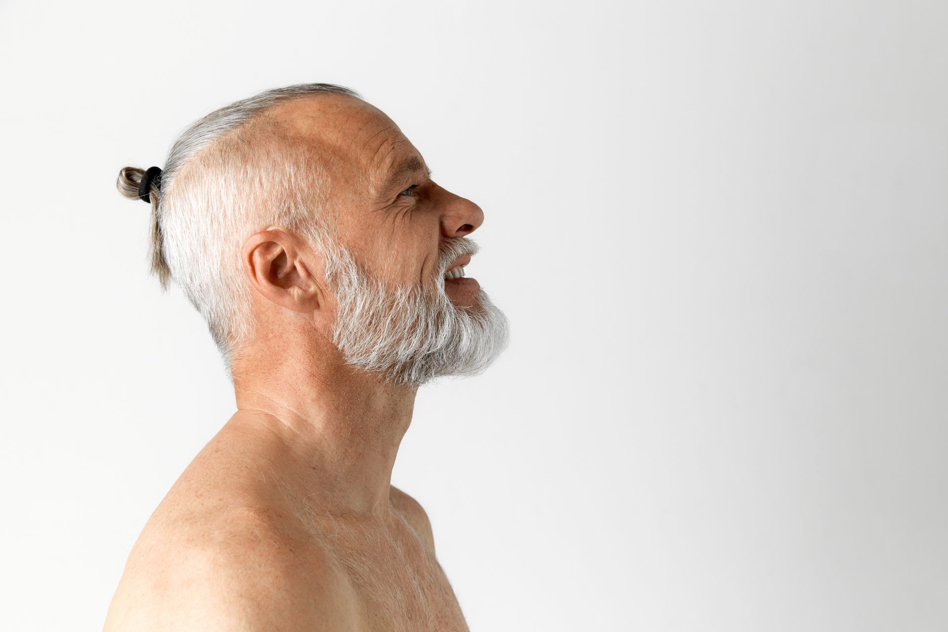 A shirtless man with a beard and ponytail is looking up.