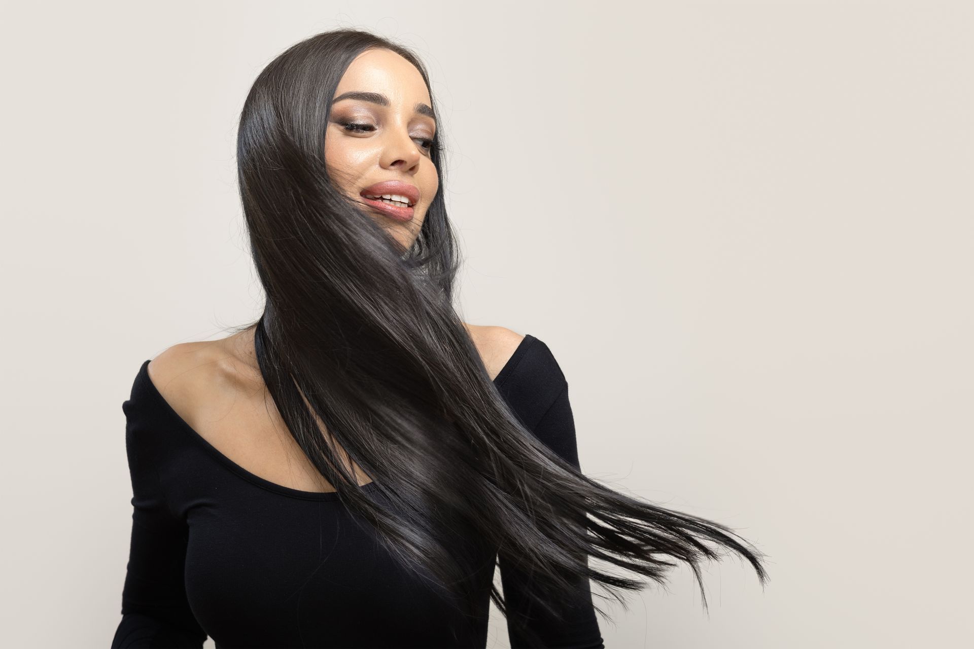 Woman with long dark hair turning her head, wearing a black top against a light background