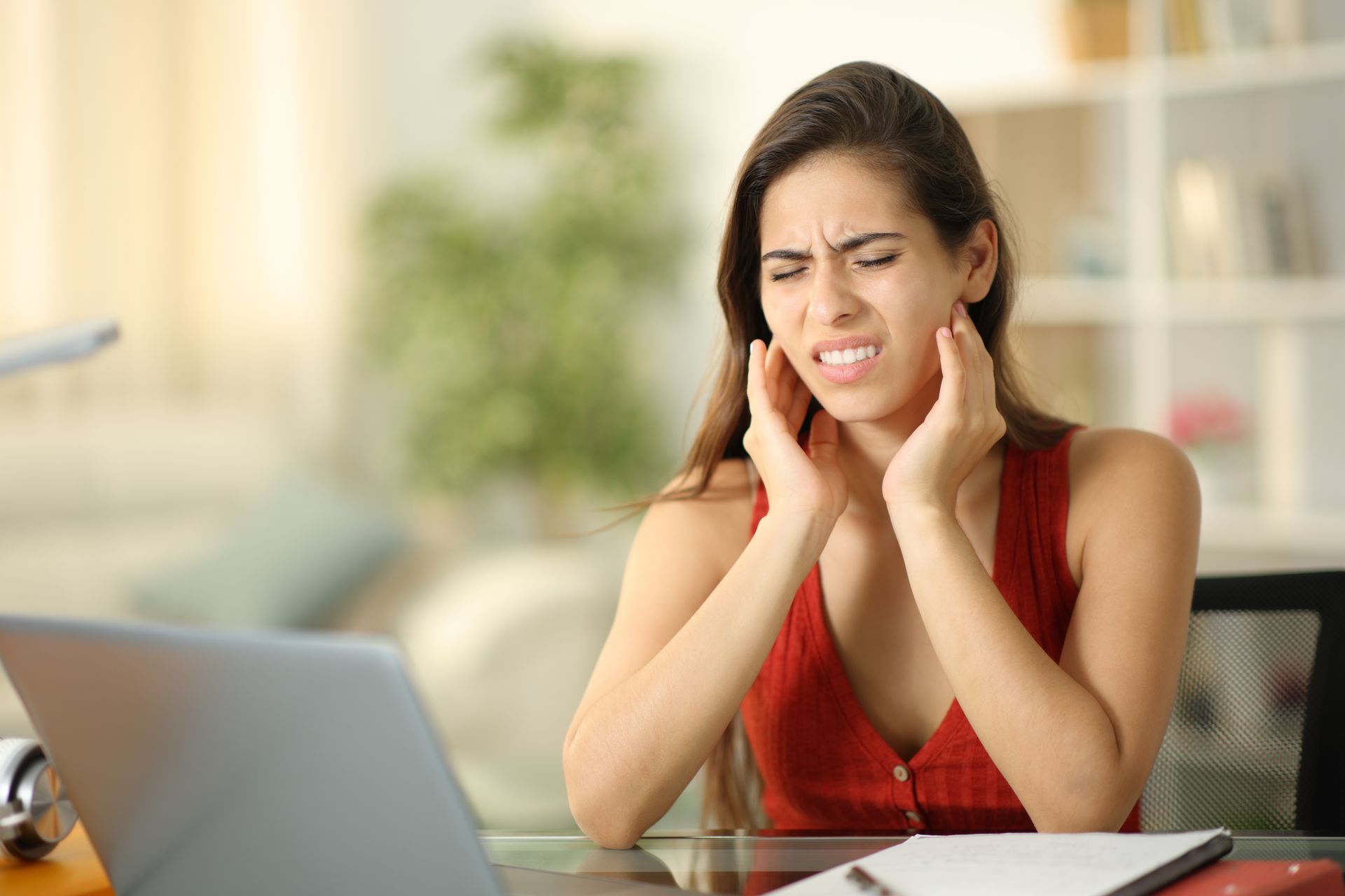 Person grimacing and holding temples beside a laptop at a desk