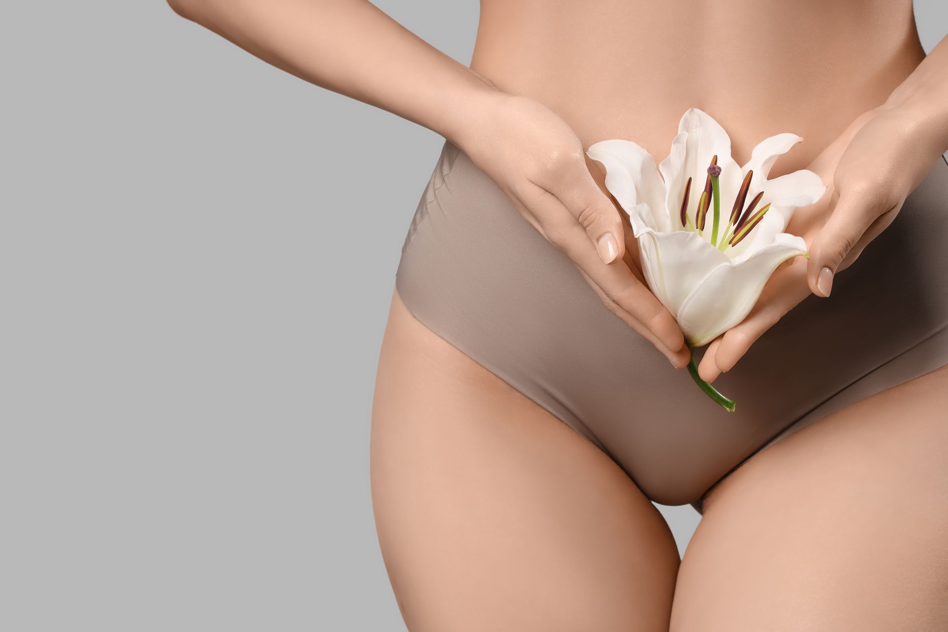 Hands holding a white flower over beige underwear on a gray background
