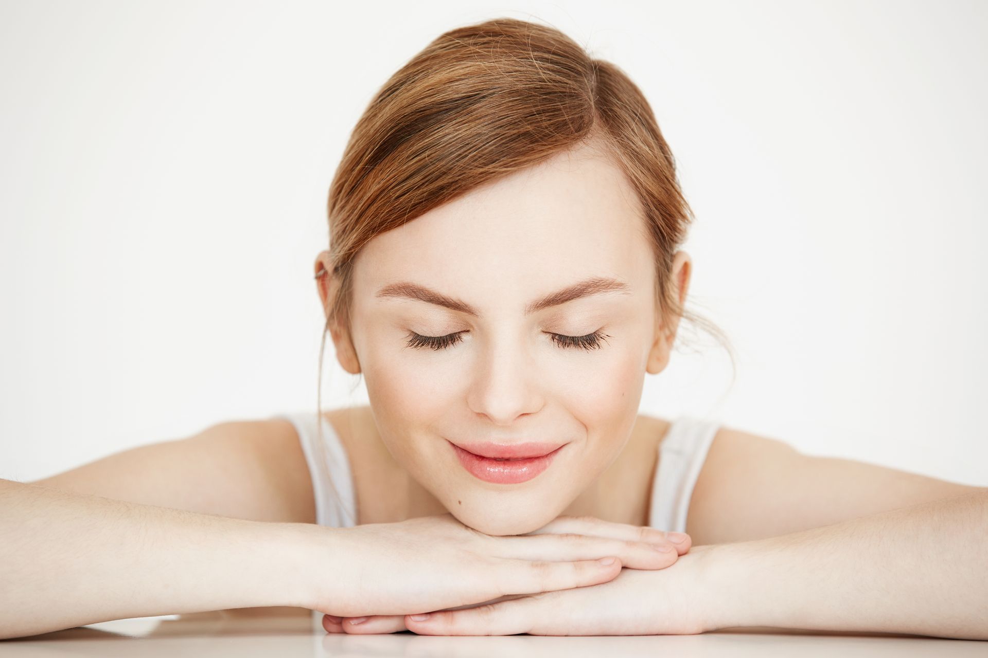 A woman is smiling with her eyes closed and her hands on her face.