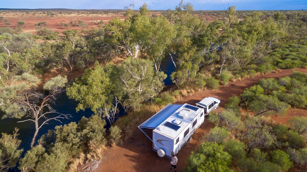 White Camper Van on a Red Dirt Track in a Green Desert Landscape — Dempsters Caravan & RV in Gin Gin, QLD