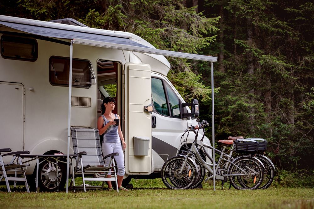 Woman Standing by a Camper Van in a Grassy Campsite — Dempsters Caravan & RV in Gin Gin, QLD